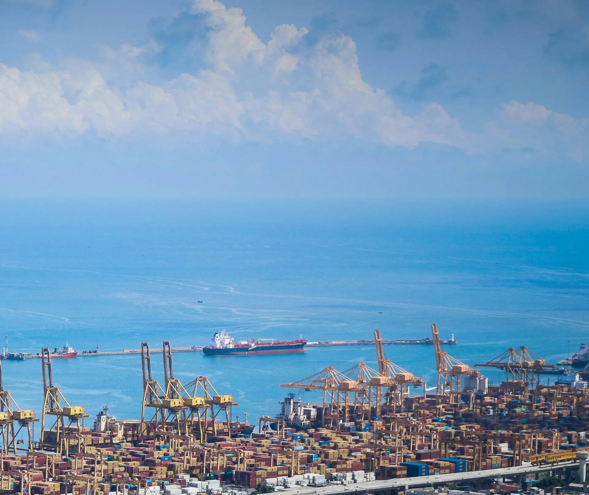 A container terminal with yellow quay cranes beside a calm blue sea under a bright sky.