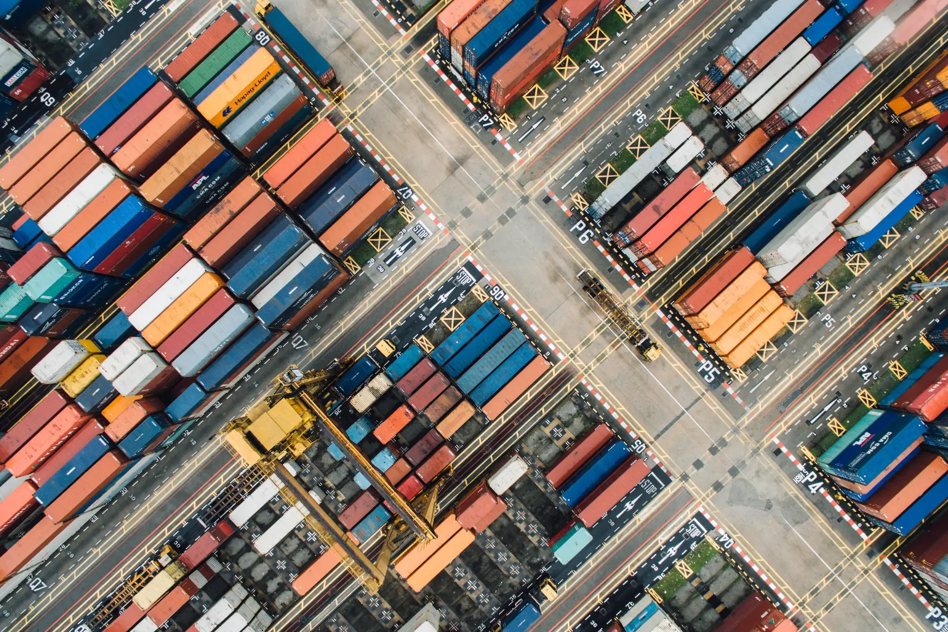 Stacks of colourful containers and yellow gantry cranes seen from directly above, laid out in a diagonal grid.