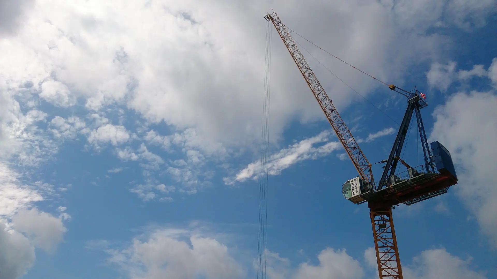 A tall tower crane against a blue sky with white clouds.