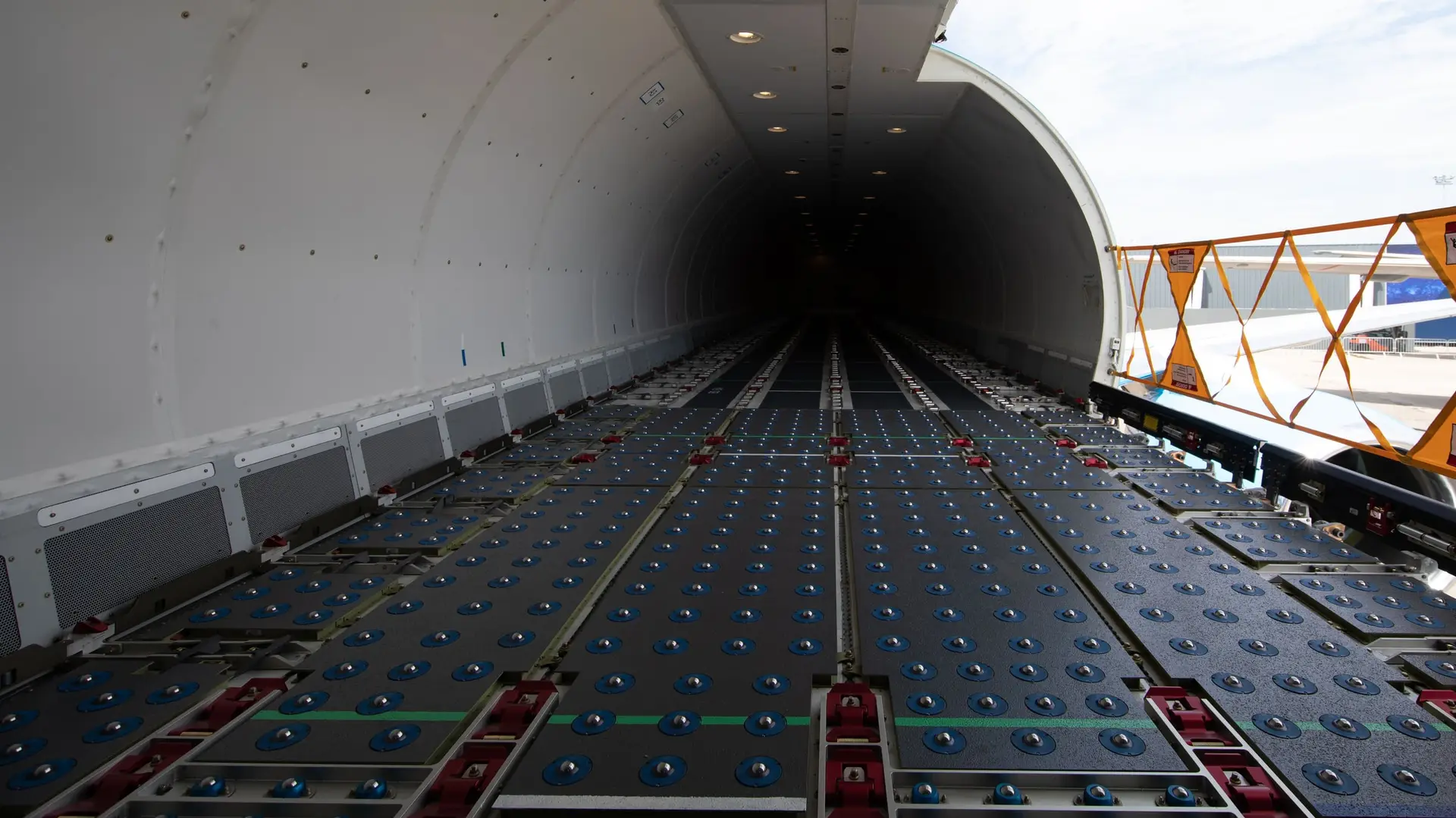 The empty main deck of a cargo aircraft, its roller floor leading to an open side cargo door in daylight.
