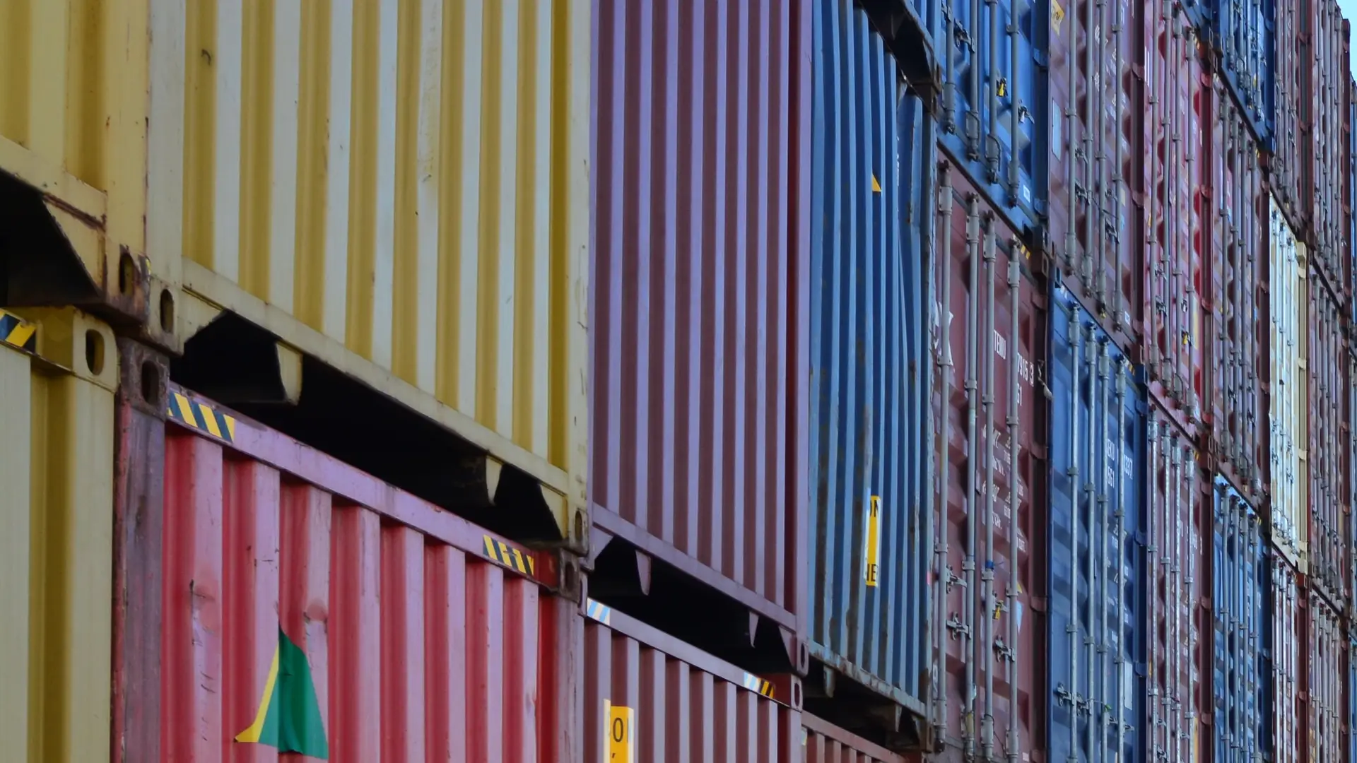 Stacks of yellow, red and blue shipping containers in bright sunlight.