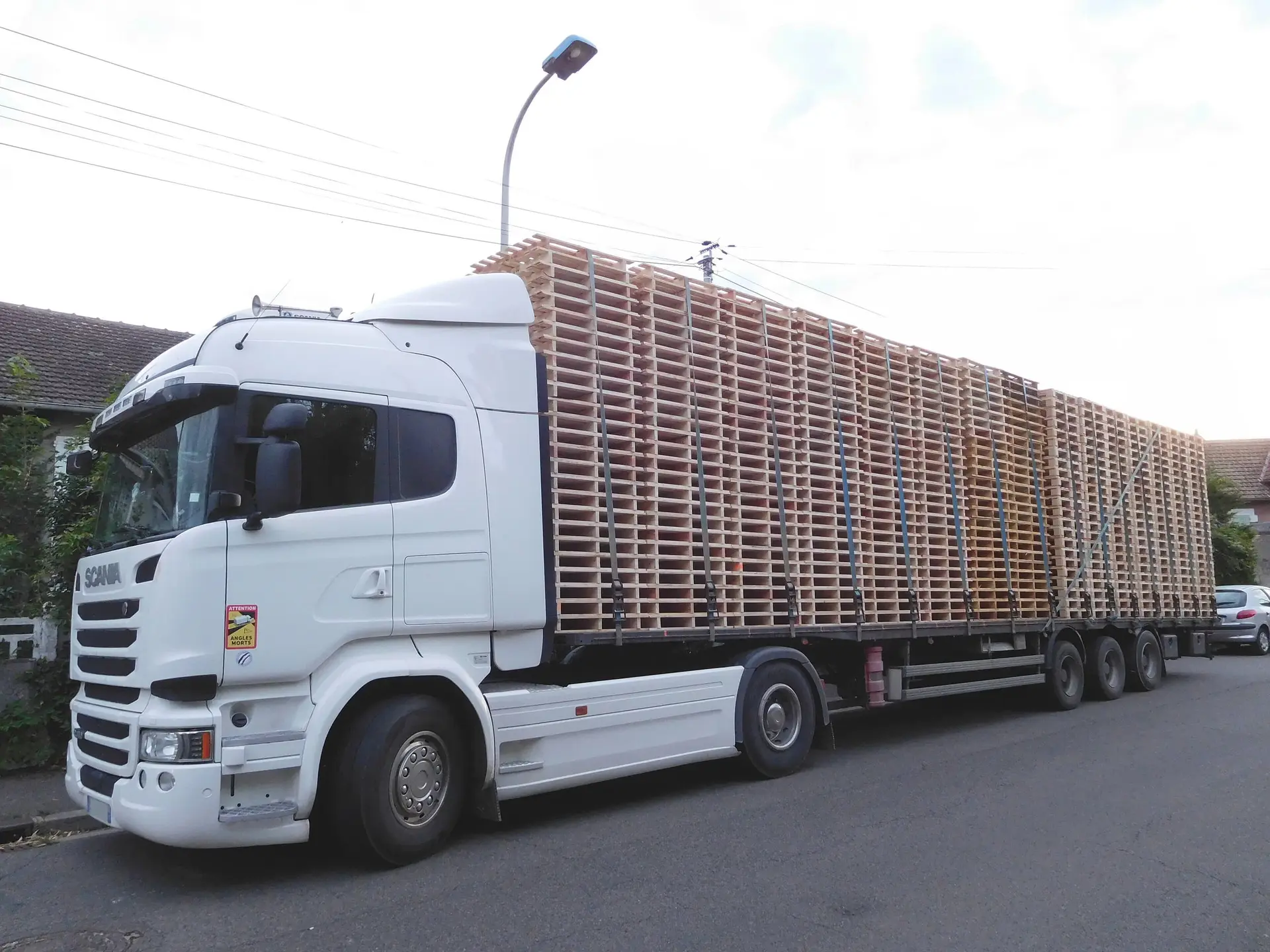 A white truck and flatbed trailer loaded high with strapped stacks of empty wooden pallets, ready for collection.