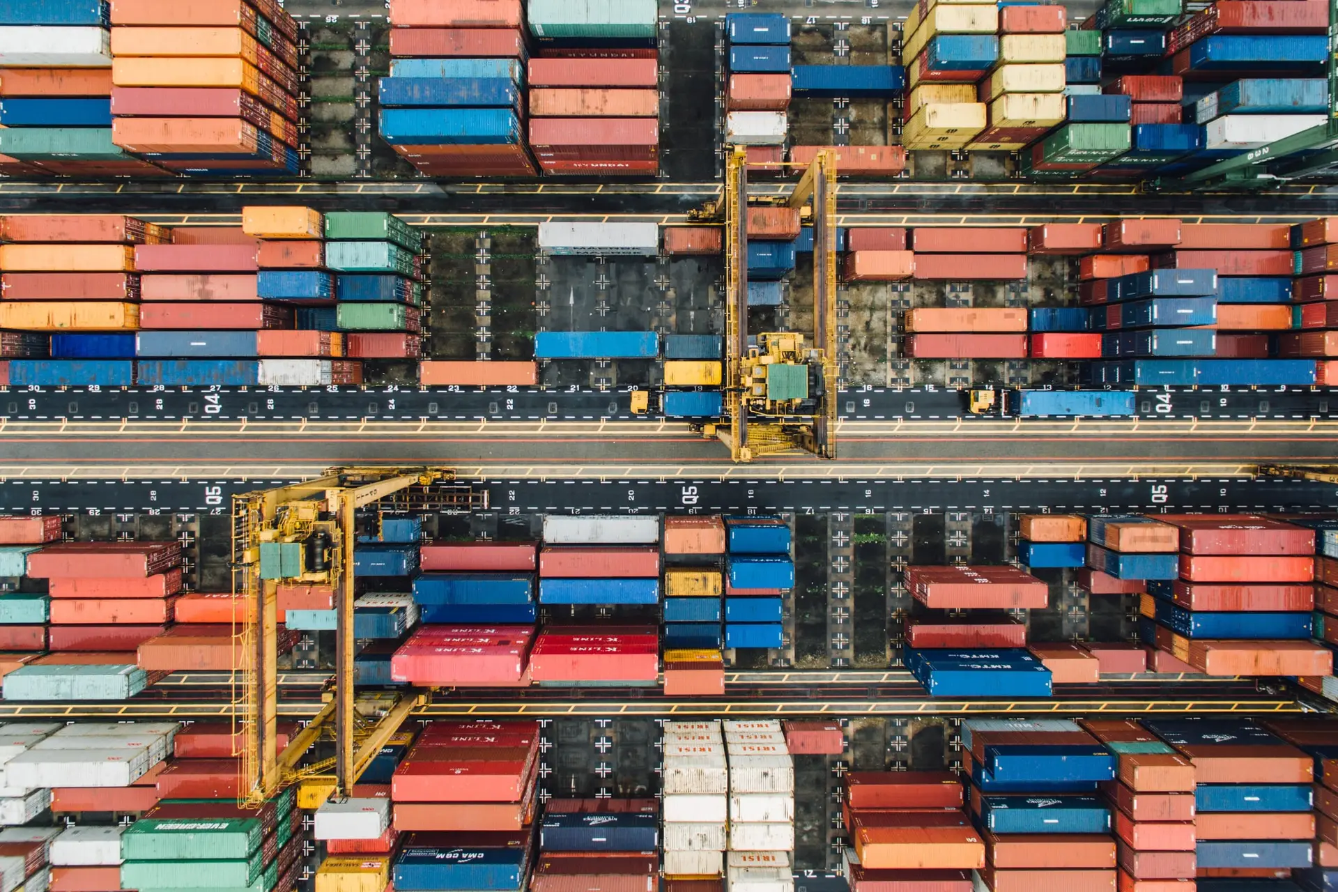 Rows of red, blue and white containers with yellow gantry cranes, seen from directly above a container terminal.